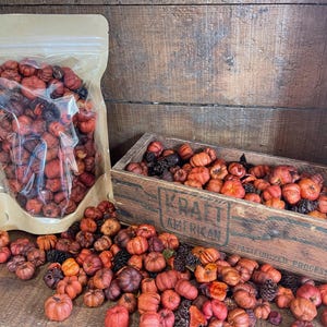 May include: A clear plastic bag filled with dried orange and brown pumpkin-shaped potpourri. A wooden crate filled with the same potpourri is in the background. The crate has the text "Kraft American" printed on the front.