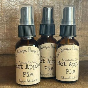 May include: Three brown glass bottles with black spray tops and labels that read "Antique Flower Factory" and "My Grandma Mary Smith's Hot Apple Pie Potpourri Refresher Oil".