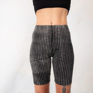 May include: High-waisted biker shorts featuring a black and white checkered pattern that transitions into vertical stripes along the legs. The garment has a fitted silhouette and reaches mid-thigh, constructed from a stretchy fabric material.