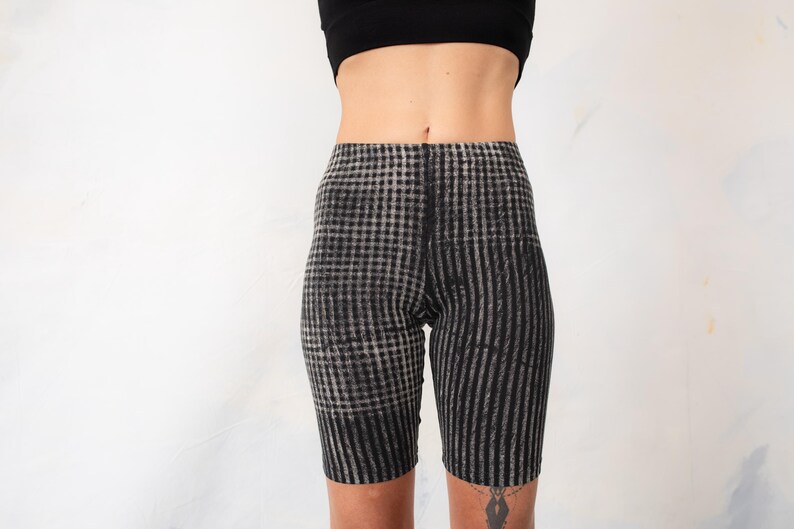 May include: High-waisted biker shorts featuring a black and white checkered pattern that transitions into vertical stripes along the legs. The garment has a fitted silhouette and reaches mid-thigh, constructed from a stretchy fabric material.