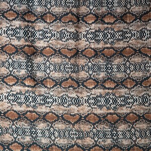 May include: A fabric with a snakeskin pattern. The design features a repeating pattern of brown, black, and cream-colored diamond shapes, creating a textured, reptile-like appearance. The fabric is likely used for clothing or accessories.