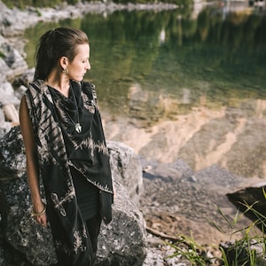 Może przedstawiać: Kobieta w czarno-białym szalu z tie-dye i srebrnym naszyjnikiem z zawieszką stoi w pobliżu zbiornika wodnego. Ma na sobie czarną bluzkę i związane włosy.