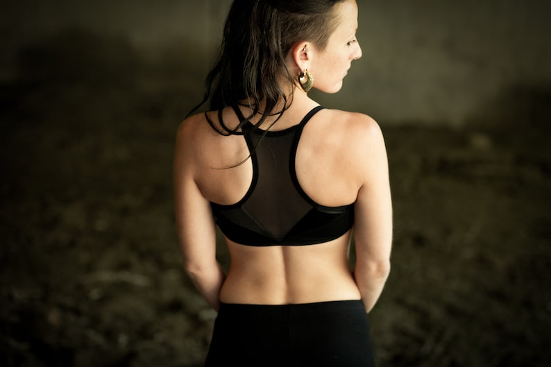 May include: A woman wearing a black sports bra with a mesh panel in the back. The bra has a racerback style and is made of a stretchy material.