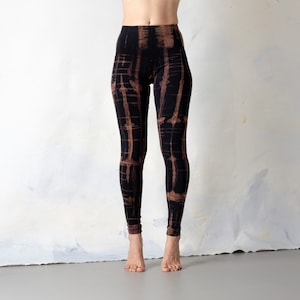 Op de afbeelding: Zwarte leggings met een bruin tie-dye patroon. De leggings zijn hoog getailleerd en hebben een aansluitende pasvorm.