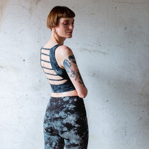Puede incluir: Una mujer con un top negro corto con un dise&ntilde;o de espalda cruzada y leggings de color negro y blanco tie-dye.