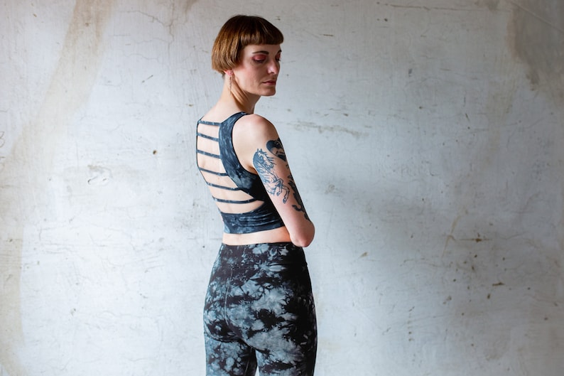 Puede incluir: Una mujer con un top negro corto con un dise&ntilde;o de espalda cruzada y leggings de color negro y blanco tie-dye.