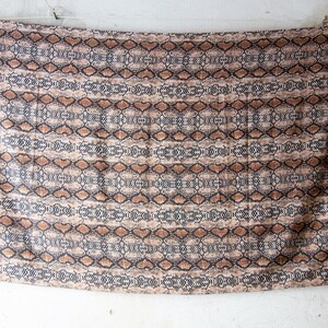 May include: A rectangular fabric with a snakeskin pattern. The design features a repeating pattern of brown, black, and tan shapes, resembling reptile scales. The fabric is hanging from a clothesline.