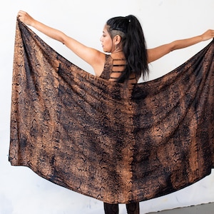 Peut inclure: Un châle à imprimé peau de serpent marron et noir est tenu ouvert, révélant un haut assorti avec des détails découpés dans le dos. Le tissu a un aspect texturé. La tenue est portée par une personne.