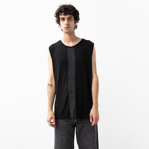 Könnte beinhalten: Ein schwarzes ärmelloses Tanktop mit einem vertikalen, strukturierten grauen Einsatz in der Mitte der Brust. Das Kleidungsstück hat einen Rundhalsausschnitt und einen geraden Saum und besteht aus leichtem Stoff mit lockerer Passform.