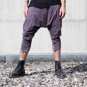 May include: A person wearing a pair of purple, cropped pants with a loose fit and a gathered detail at the crotch. They are wearing black lace-up boots.