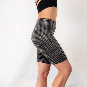 May include: High-waisted biker shorts featuring a black and grey checkered pattern. The shorts have a fitted silhouette that extends to the mid-thigh, showcasing a consistent grid design throughout the fabric, paired with a black athletic top.
