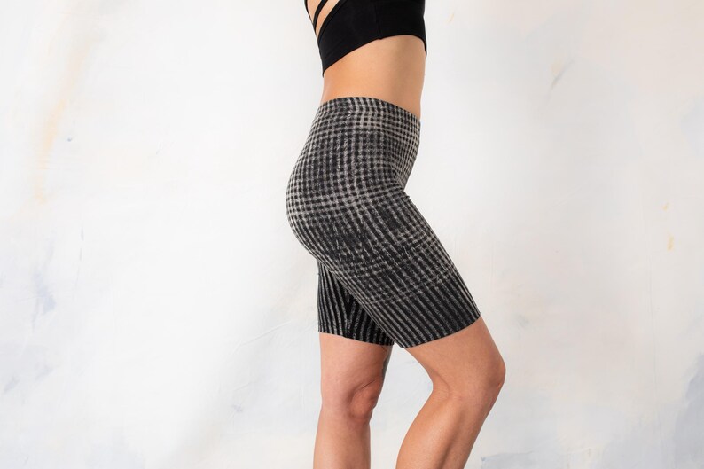 May include: High-waisted biker shorts featuring a black and grey checkered pattern. The shorts have a fitted silhouette that extends to the mid-thigh, showcasing a consistent grid design throughout the fabric, paired with a black athletic top.