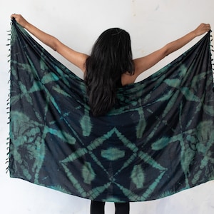 Può includere: Una persona indossa un pareo in tie-dye nero e verde con frange. Il pareo è tenuto davanti alla persona, mostrando il complesso motivo a tie-dye.