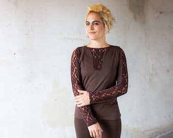 May include: A long-sleeved brown shirt featuring intricate lace detailing on the sleeves and a matching lace panel at the center of the neckline. The garment has a round neck and a fitted silhouette, crafted from a solid brown fabric.