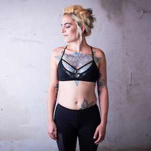 May include: A woman with blonde hair and tattoos wearing a black sports bra with a mesh design and black leggings.