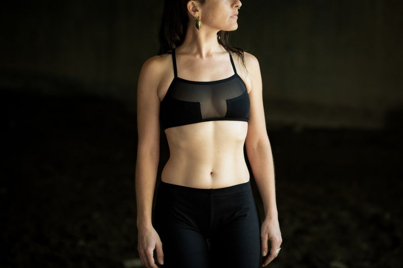 May include: A woman wearing a black sports bra with a sheer mesh panel and black leggings.