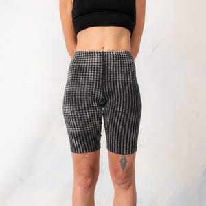 May include: High-waisted biker shorts featuring a black and grey pattern. The left leg displays a checkered design, while the right leg features vertical stripes. These form-fitting shorts reach mid-thigh and have a seamless, elasticized waistband.
