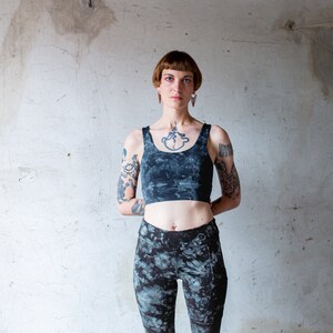Puede incluir: Una mujer con el pelo corto y casta&ntilde;o oscuro y tatuajes en los brazos lleva un top corto azul oscuro y leggings a juego. El top tiene un estampado tie-dye y los leggings tienen un estampado similar.