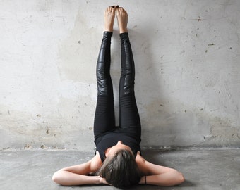 May include: Black leggings featuring a matte fabric base with vertical panels of glossy, leather-like material running down the front of the legs. The leggings have a fitted silhouette with ribbed detailing at the knees and a solid black waistband.