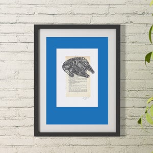 K&ouml;nnte beinhalten: Eine Schwarzwei&szlig;illustration des Raumschiffs Millennium Falcon aus Star Wars, gedruckt auf einer Buchseite. Das Bild ist in einem schwarzen Rahmen mit einer blauen Passepartout gerahmt.