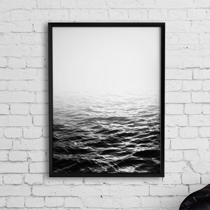 May include: Black and white photograph of a foggy ocean scene. The water is choppy and the sky is overcast. The image is framed in a black frame.