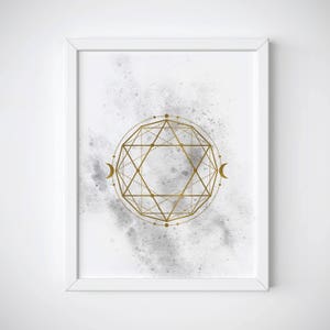 May include: A white framed print with a gold geometric design on a gray watercolor background. The design features a circle with a star inside and two crescent moons on either side.