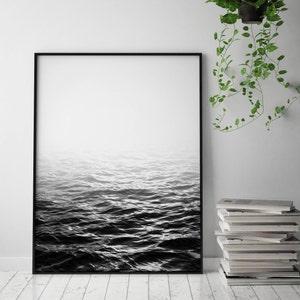 May include: Black and white photograph of a wavy ocean with a foggy sky. The image is framed in a black frame.