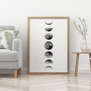 May include: A black and white print of the moon in various phases, framed in a light wood frame. The print is hanging on a white wall in a living room setting.