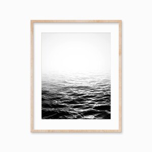 May include: A black and white photograph of a rippling ocean surface with a bright white sky above.
