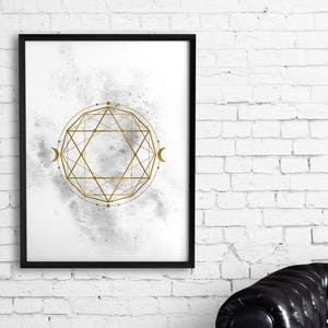 May include: A black framed print with a white background and a gold geometric design. The design is a circle with a star inside and a crescent moon on each side. The background is a watercolor wash of gray and white.