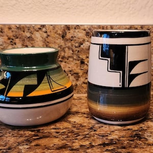 May include: Two ceramic vases with geometric patterns. The larger vase is white with black and green geometric designs. The smaller vase is white with black, green, and yellow geometric designs.