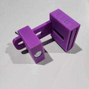 May include: A purple 3D printed plastic clamp with a metal screw and a label that reads "1 mm".