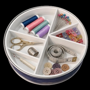 May include: A round white plastic sewing organizer tray with blue sides containing four spools of thread, a set of colorful ball-head pins, plastic sewing clips, a gold-tone metal thimble, gold scissors, a seam ripper, and a measuring tape.