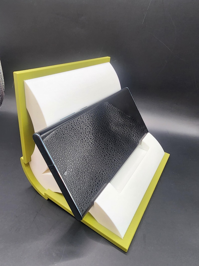 May include: A black phone case with a textured surface is displayed on a green and white phone stand.