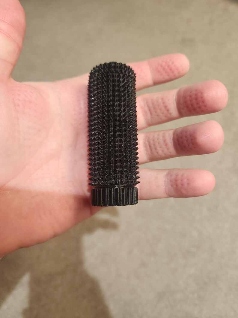 May include: A black, cylindrical object with a textured surface covered in small, pointed protrusions. The object has a ridged base and a rough, spiky appearance. The item is held in a hand.
