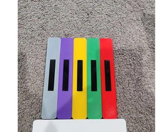 May include: A set of six colorful wooden blocks with black keys, resembling a miniature piano. The blocks are arranged in a row, with the colors gray, purple, yellow, green, and red.