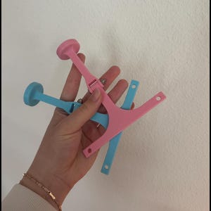 Puede incluir: Dos pinzas para el pelo de pl&aacute;stico, una rosa y otra azul, con un extremo redondeado y un dise&ntilde;o en forma de Y. Las pinzas se sostienen en una mano.