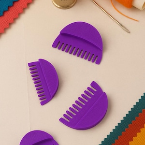 May include: A collection of sewing tools and supplies, including four purple thread combs, a gold thimble, a needle, and orange thread. Colorful fabric swatches in teal, red, and orange are also visible.