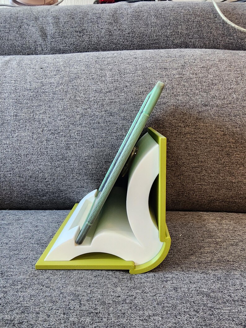 May include: A green tablet stand made of plastic, shaped like an open book. The stand is designed to hold a tablet in an upright position, allowing for easy viewing.