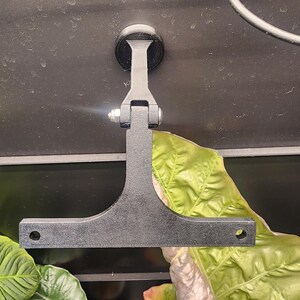 Puede incluir: Soporte de pared de metal negro con una base de ventosa y un brazo en forma de T. El soporte est&aacute; dise&ntilde;ado para sujetar un dispositivo u objeto.