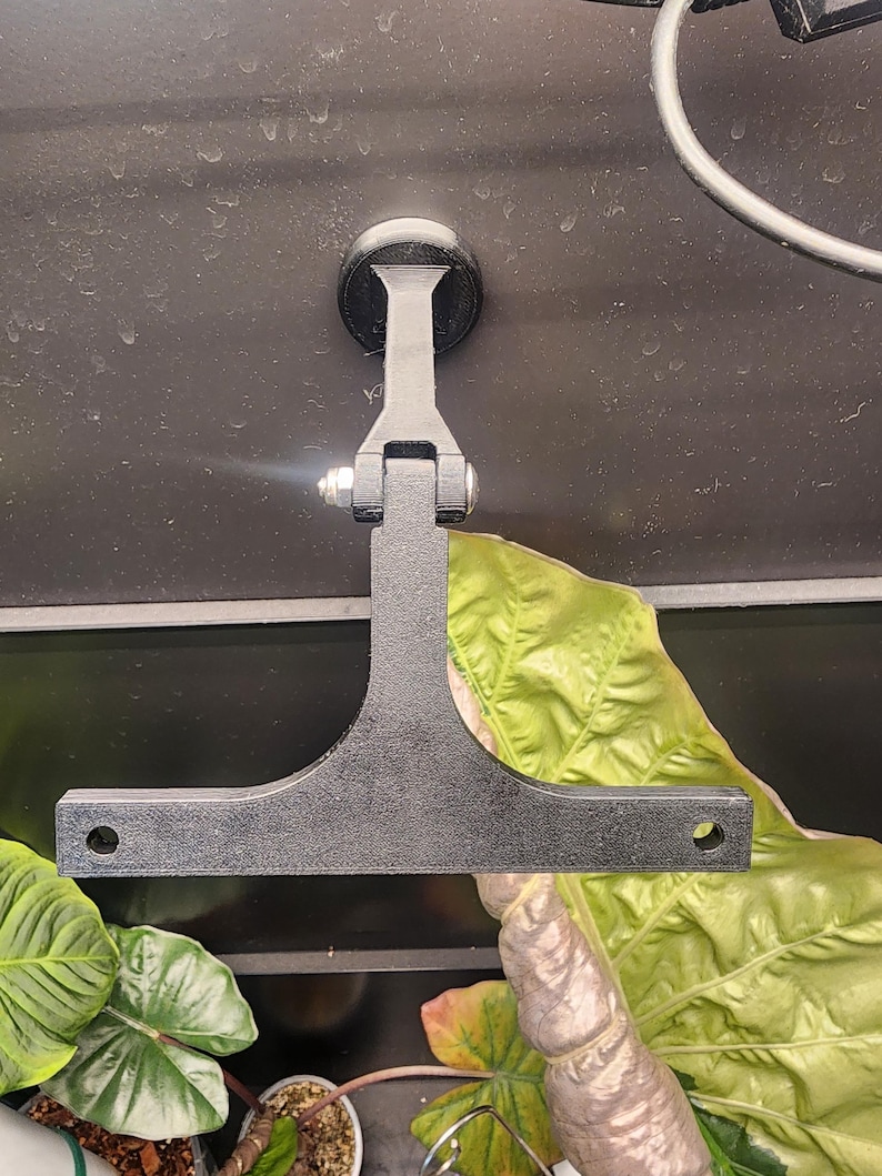 Puede incluir: Soporte de pared de metal negro con una base de ventosa y un brazo en forma de T. El soporte est&aacute; dise&ntilde;ado para sujetar un dispositivo u objeto.
