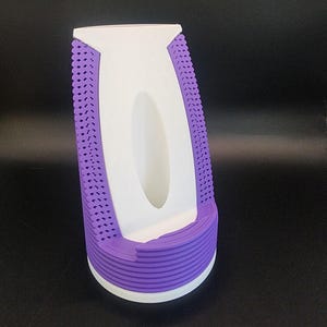 May include: A white and purple phone stand with a textured design. The stand has a raised lip to hold a phone in place.