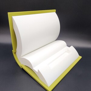 May include: A white book-shaped display stand with a yellow border. The stand is open and has a slot in the middle.