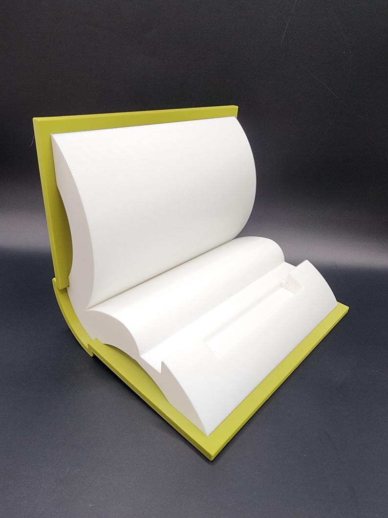 May include: A white book-shaped display stand with a yellow border. The stand is open and has a slot in the middle.
