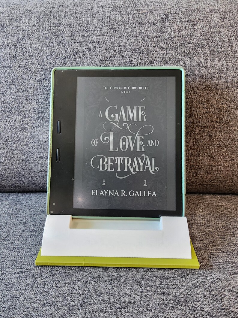 May include: A green e-reader displaying the cover of a book titled "A Game of Love and Betrayal" by Elayna R. Gallea. The book is part of a series called "The Choosing Chronicles".