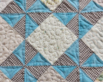 May include: A quilt with a geometric pattern of blue and gray squares and triangles. The quilt is made of different fabrics with floral and geometric designs.