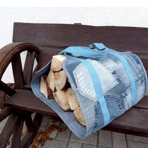 May include: A blue denim firewood carrier with a light blue strap. The carrier is filled with a stack of firewood logs.