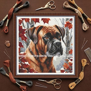 Puede incluir: Un retrato en punto de cruz enmarcado de un perro Boxer con pelaje marrón y negro, sobre un fondo de hojas de otoño y un bosque nevado. La imagen está rodeada de suministros de bordado, incluyendo hilo, tijeras y agujas.