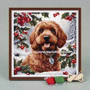 May include: Framed cross-stitch of a brown dog with a silver tag, surrounded by holly and snow. The dog is smiling with its tongue out. The frame is brown. Includes red and green thread spools and a bone-shaped needle holder.