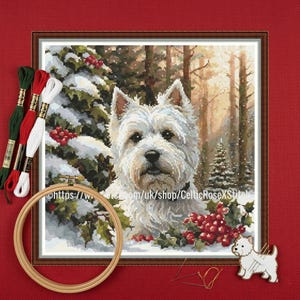 May include: Cross-stitch of a Westie dog in a snowy forest, with holly and berries. The image is framed and surrounded by embroidery threads, a wooden hoop, and a dog-shaped pin.
